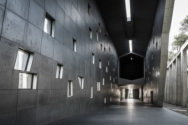 نمای داخلی موزه یهود برلین با دیوارهای بتنی خاکستری بلند، راهروی طولانی و پنجرههای کوچک و نامنظم که نوری اندک و زاویهدار را به فضای سرد و مدرن داخلی میتابانند.