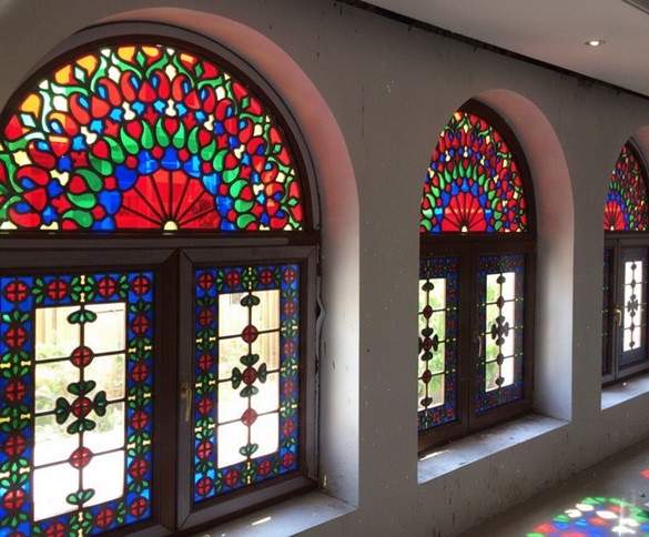 ردیفی از پنجرههای ارسی با شیشههای رنگی قرمز، آبی، سبز و زرد و طرحهای هندسی اسلیمی که نور خورشید را به صورت رنگارنگ روی کف زمین بازتاب دادهاند.