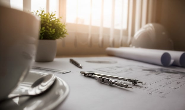 میز کار مهندسی با تجهیزات نقشه‌خوانی حرفه‌ای شامل پرگار، نقشه‌های لوله شده و کلاه ایمنی